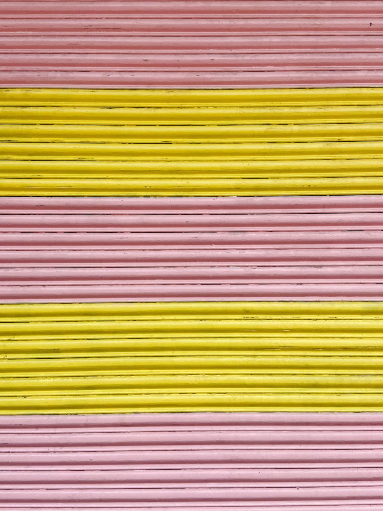 Close up photograph of the texture of a garage door that is painted in pink and yellow stripes