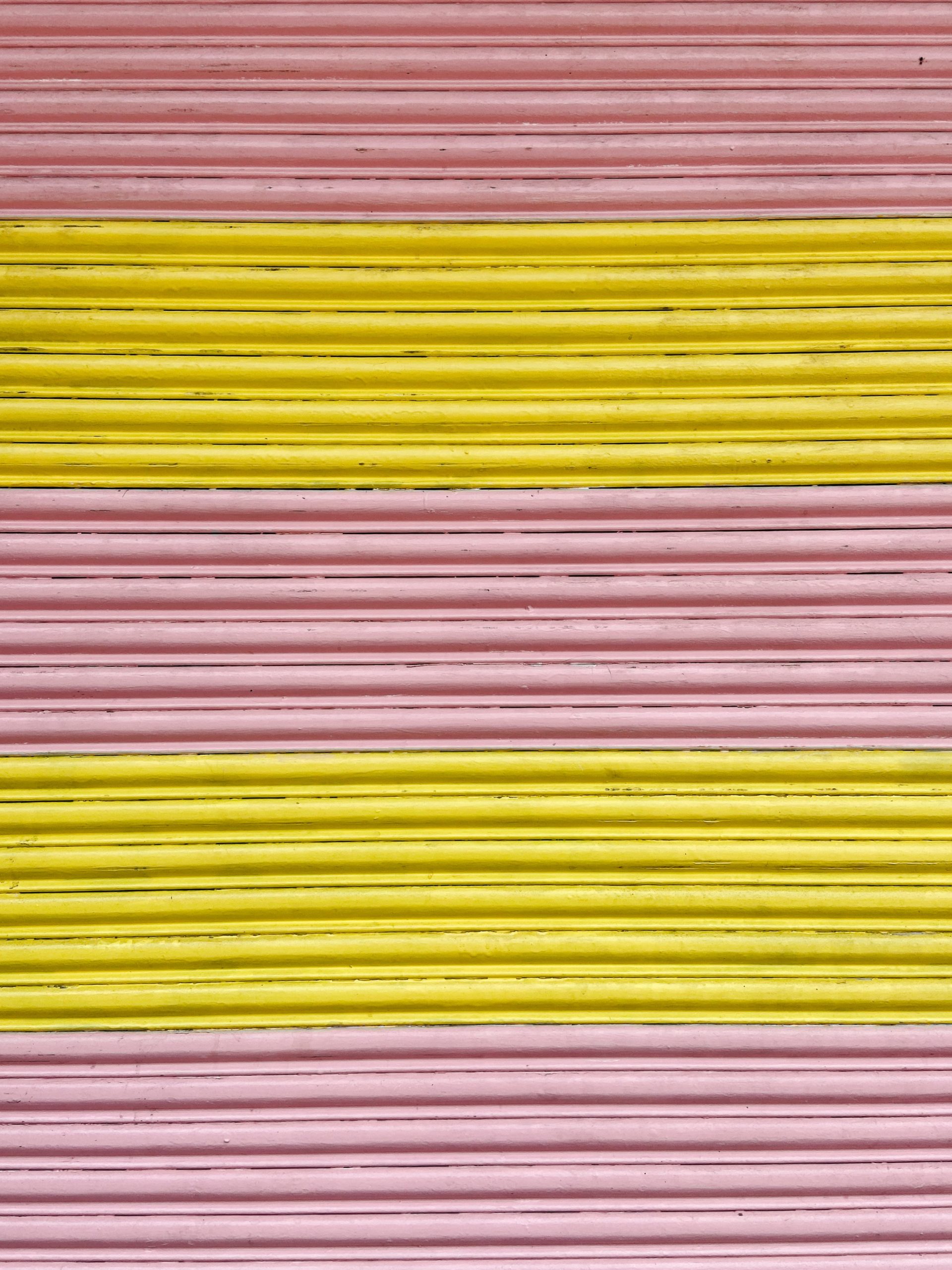 Close up photograph of the texture of a garage door that is painted in pink and yellow stripes